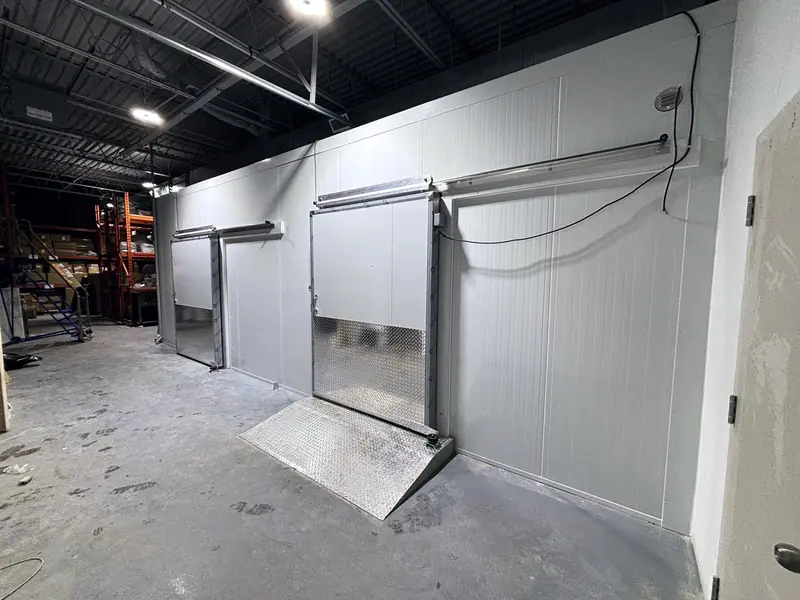 Combination walk-in cooler and freezer with two sliding doors and diamond-plate ramps inside a warehouse